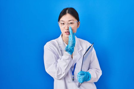 Photo for Chinese young woman working at scientist laboratory hand on mouth telling secret rumor, whispering malicious talk conversation - Royalty Free Image