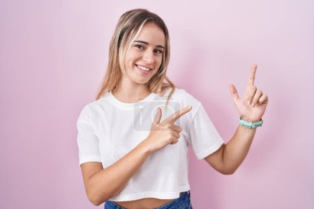 Téléchargez les photos : Jeune femme blonde debout sur fond rose souriant et regardant la caméra pointant avec deux mains et doigts sur le côté. - en image libre de droit