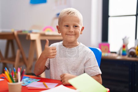 Photo for Little caucasian boy painting at the school smiling happy and positive, thumb up doing excellent and approval sign - Royalty Free Image