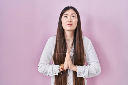 Photo for Chinese young woman standing over pink background begging and praying with hands together with hope expression on face very emotional and worried. begging. - Royalty Free Image