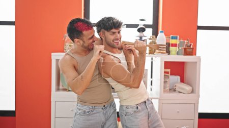 Foto de Dos hombres pareja cantando canción usando utensilio de cocina como micrófono en el comedor - Imagen libre de derechos