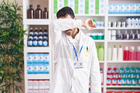 Photo for Handsome hispanic man working at pharmacy drugstore covering eyes with arm, looking serious and sad. sightless, hiding and rejection concept - Royalty Free Image