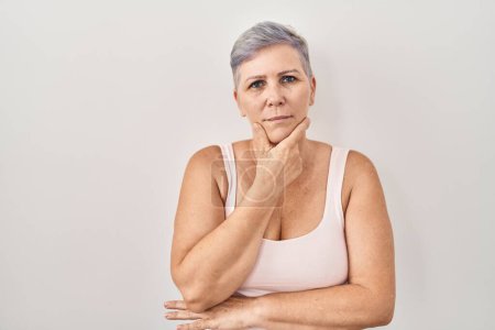 Foto de Middle age caucasian woman standing over white background looking confident at the camera smiling with crossed arms and hand raised on chin. thinking positive. - Imagen libre de derechos