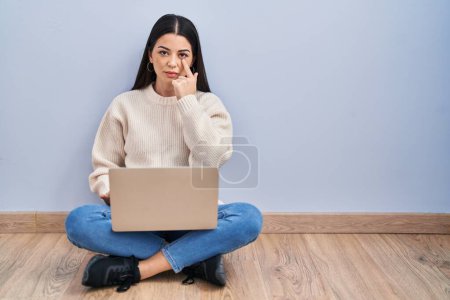 Photo for Young woman using laptop sitting on the floor at home pointing to the eye watching you gesture, suspicious expression - Royalty Free Image