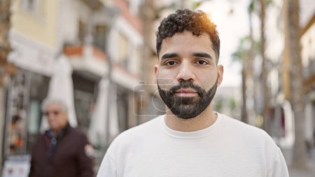 Téléchargez les photos : Jeune homme hispanique debout avec une expression sérieuse dans la rue - en image libre de droit