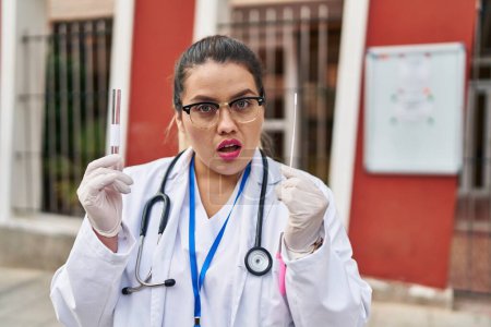 Téléchargez les photos : Jeune médecin hispanique femme faisant coronavirus infection nasale test expression désemparée et confus. concept de doute. - en image libre de droit