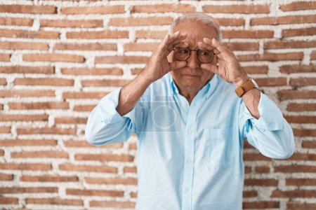 Téléchargez les photos : Homme âgé avec les cheveux gris debout sur le mur de briques essayant d'ouvrir les yeux avec les doigts, somnolent et fatigué pour la fatigue matinale - en image libre de droit