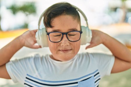 Photo for Adorable hispanic boy listening to music at park - Royalty Free Image