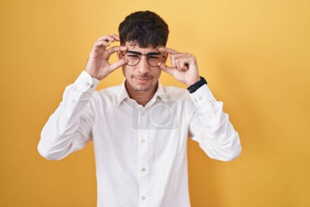 Téléchargez les photos : Jeune homme hispanique debout sur fond jaune essayant d'ouvrir les yeux avec les doigts, somnolent et fatigué pour la fatigue matinale - en image libre de droit