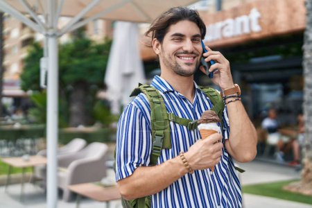 Photo for Young hispanic man tourist talking on smartphone eating ice cream at street - Royalty Free Image