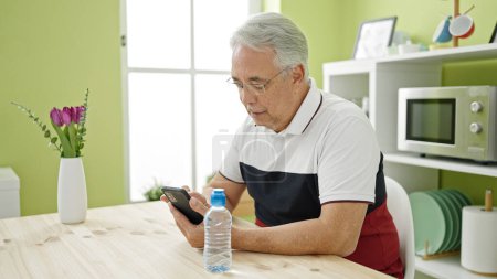 Photo for Middle age man with grey hair using smartphone sitting on the table at dinning room - Royalty Free Image
