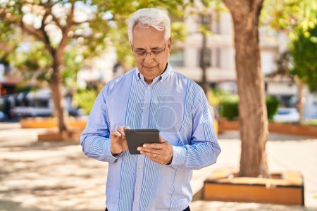 Photo for Senior man smiling confident using touchpad at park - Royalty Free Image