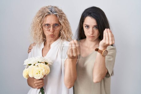 Foto de Madre e hija sosteniendo ramo de flores blancas haciendo gesto italiano con la mano y los dedos expresión confiada - Imagen libre de derechos