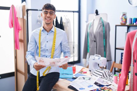 Téléchargez les photos : Jeune homme hispanique tailleur souriant confiant design de vêtements à la boutique de tailleur - en image libre de droit