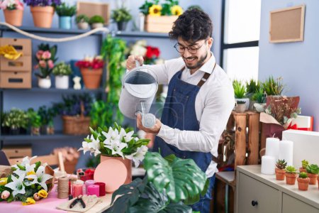 Téléchargez les photos : Young hispanic man florist smiling confident watering flowers at florist shop - en image libre de droit