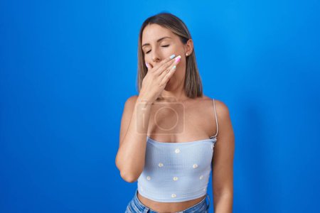Téléchargez les photos : Young woman standing over blue background bored yawning tired covering mouth with hand. restless and sleepiness. - en image libre de droit