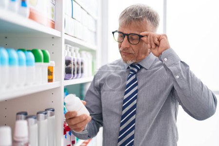 Téléchargez les photos : Moyen-âge homme aux cheveux gris client lecture des pilules étiquette au laboratoire - en image libre de droit