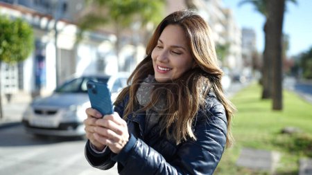 Foto de Joven hermosa mujer hispana sonriendo confiada usando teléfono inteligente en el parque - Imagen libre de derechos