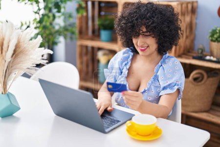 Téléchargez les photos : Jeune femme du Moyen-Orient utilisant ordinateur portable et carte de crédit à la maison - en image libre de droit