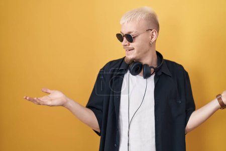 Photo for Young caucasian man wearing sunglasses standing over yellow background smiling showing both hands open palms, presenting and advertising comparison and balance - Royalty Free Image
