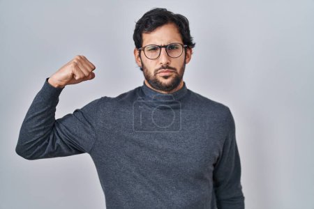 Foto de Hombre latino guapo de pie sobre un fondo aislado persona fuerte que muestra el músculo del brazo, confiado y orgulloso de poder - Imagen libre de derechos