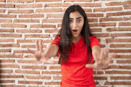 Téléchargez les photos : Jeune adolescente debout sur un mur de briques faisant un geste d'arrêt avec les mains paumes de la main, expression de colère et de frustration - en image libre de droit
