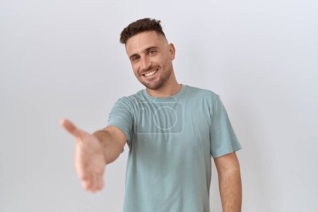 Foto de Hispanic man with beard standing over white background smiling friendly offering handshake as greeting and welcoming. successful business. - Imagen libre de derechos