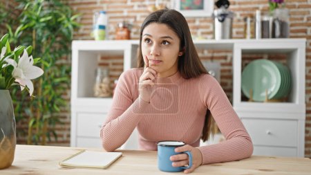 Photo for Young beautiful hispanic woman sitting on table thinking at dinning room - Royalty Free Image