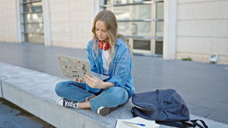 Foto de Joven estudiante rubia usando portátil sentado en el banco de la universidad - Imagen libre de derechos