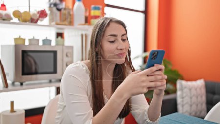 Téléchargez les photos : Jeune belle femme hispanique utilisant smartphone assis sur la table à manger - en image libre de droit