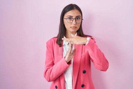 Foto de Mujer hispana joven usando ropa de negocios y gafas haciendo un gesto de tiempo fuera con las manos, rostro frustrado y serio - Imagen libre de derechos