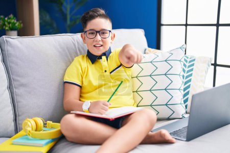 Photo for Young hispanic kid doing homework sitting on the sofa pointing displeased and frustrated to the camera, angry and furious with you - Royalty Free Image