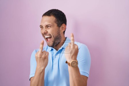 Foto de Hispanic man standing over pink background showing middle finger doing fuck you bad expression, provocation and rude attitude. screaming excited - Imagen libre de derechos