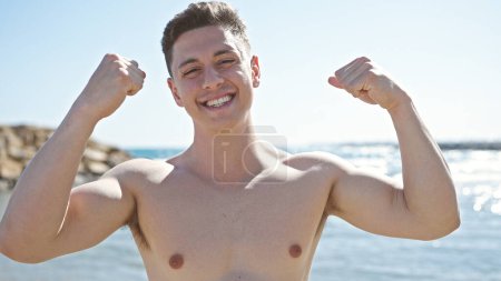 Foto de Joven turista hispano sonriendo confiado haciendo un fuerte gesto en la playa - Imagen libre de derechos