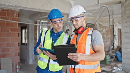 Photo for Two men builders reading document using touchpad shake hands at construction site - Royalty Free Image