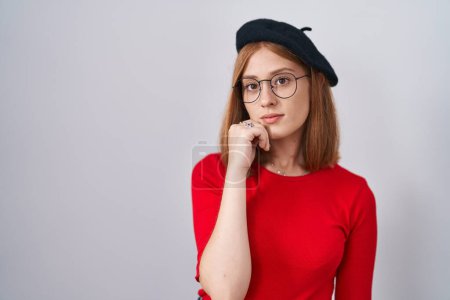 Photo for Young redhead woman standing wearing glasses and beret with hand on chin thinking about question, pensive expression. smiling with thoughtful face. doubt concept. - Royalty Free Image