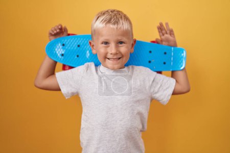 Téléchargez les photos : Petit garçon caucasien tenant le skate souriant avec un sourire heureux et cool sur le visage. montrant les dents. - en image libre de droit