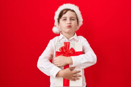 Téléchargez les photos : Petit garçon caucasien portant un chapeau de Noël et tenant des cadeaux regardant la caméra souffler un baiser étant charmant et sexy. expression d'amour. - en image libre de droit