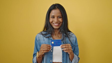 Foto de Mujer afroamericana sonriendo confiada sosteniendo tarjeta de crédito sobre fondo amarillo aislado - Imagen libre de derechos