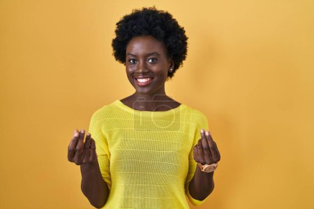 Photo for African young woman standing over yellow studio doing money gesture with hands, asking for salary payment, millionaire business - Royalty Free Image