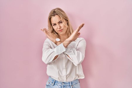 Téléchargez les photos : Jeune femme caucasienne portant une chemise blanche décontractée sur fond rose expression de rejet croisant les bras faisant signe négatif, visage en colère - en image libre de droit