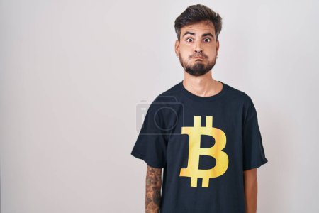 Photo for Young hispanic man with tattoos wearing bitcoin t shirt puffing cheeks with funny face. mouth inflated with air, crazy expression. - Royalty Free Image