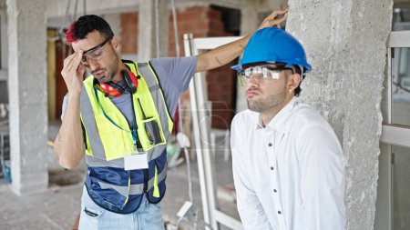 Foto de Dos hombres constructor y arquitecto de pie junto con la expresión estresada en el sitio de construcción - Imagen libre de derechos