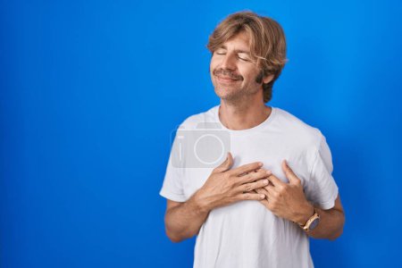 Photo for Middle age man standing over blue background smiling with hands on chest with closed eyes and grateful gesture on face. health concept. - Royalty Free Image