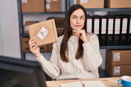 Photo for Young brunette woman working at small business ecommerce serious face thinking about question with hand on chin, thoughtful about confusing idea - Royalty Free Image