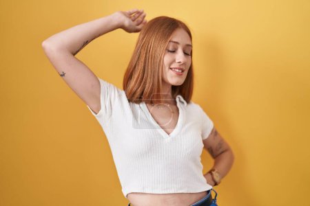 Photo for Young redhead woman standing over yellow background stretching back, tired and relaxed, sleepy and yawning for early morning - Royalty Free Image