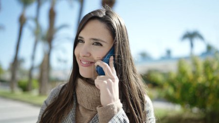 Foto de Hermosa mujer hispana sonriendo confiada hablando en el teléfono inteligente del parque - Imagen libre de derechos