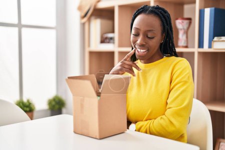 Photo for Beautiful black woman opening cardboard box smiling looking confident at the camera with crossed arms and hand on chin. thinking positive. - Royalty Free Image