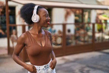 Téléchargez les photos : Femme africaine avec les cheveux bouclés à l'extérieur de la ville portant des écouteurs regardant la caméra souffler un baiser étant belle et sexy. expression d'amour. - en image libre de droit