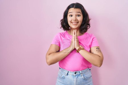 Photo for Young hispanic woman standing over pink background praying with hands together asking for forgiveness smiling confident. - Royalty Free Image